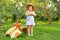 Portrait of children in apple orchard. Little girl in straw hat, blue striped dress, holding wicker basket with apples