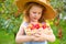 Portrait of children in an apple orchard. Little girl in straw hat and blue striped dress, holding wicker basket with apples. Care