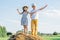 Portrait of children boy and girl spreading and waving arms, playing the ape on haystack in field. Wearing straw hats