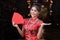 Portrait of Chinese woman wear traditional dress cheongsam and holding Red envelope or gife voucher for reward at chinese shrine