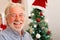 Portrait and close up of old mature man smiling and laughing looking at the camera with a christmas tree at the background - old