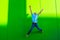 Portrait and close up of teenager or millennial or young man jumping having fun and listening music with headphones - green