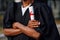 Portrait closeup of black man graduate from university stand outdoors in mantle with crossed arms and holding higher