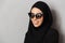 Portrait closeup of muslim fashion woman 20s in religious headscarf and sunglasses smiling and looking aside, isolated over gray