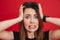 Portrait closeup of nervous woman grabbing her head and expressing problem or fright, isolated over red background