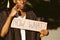 Portrait closeup of upset unemployed black guy standing with cardboard poster on street looking for job. University or