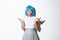 Portrait of clueless young asian party girl in blue wig shrugging, looking indecisive at camera, standing over white