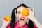 Portrait of comic happy girl holding orange near face gray background