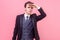 Portrait of concentrated attentive young businessman in tuxedo holding hand over head. indoor studio shot isolated on pink