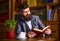 Portrait of concentrated bearded man holding open book and drinking tea.