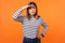 Portrait of concentrated curious young woman with brown hair in long sleeve striped shirt. indoor studio shot isolated on orange