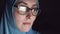 Portrait of concentrated face of Muslim woman in hijab and glasses at night in the dark searches the Internet