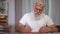 Portrait of concentrated senior bearded man writing diary sitting at table indoors. Front view medium shot of confident