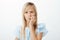 Portrait of concerned focused little girl with long blond hair, folding lips and biting fingers, staring at camera