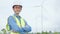 Portrait of confident Asian engineer arms crossed at wind farm power station, wind turbine in background