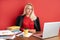 Portrait of confident caucasian blonde female sitting at office desk with laptop and papers