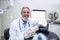 Portrait of confident dentist sitting beside chair