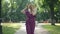 Portrait confident joyful slim woman in elegant purple jumpsuit and straw hat strolling in sunlight in summer park