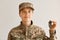 Portrait of confident young adult woman soldier wearing camouflage uniform and cap, standing and looking at camera and holding