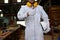 Portrait of confident young carpenter in white uniform showing thump up with pencil tools in carpentry workshop.