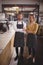 Portrait of confident young wait staff standing with arms crossed by counter