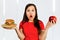Portrait confused choice think woman holds burger and red apple and surprised