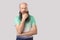 Portrait of confused middle aged bald man with long beard in light green t-shirt standing with hand on chin and looking away and