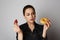 Portrait of a confused smiling caucasian woman choosing between donut and red strawberry isolated over white background.