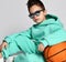 Portrait of cool handsome kid boy in pastel modern green, mint color sportswear hoodie and pants sitting with basketball