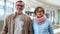 Portrait of a couple of pensioners at the airport or train station. A man and a woman with glasses look kindly at the