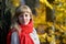 Portrait of the courageous young woman with a red scarf against the background of an autumn tree