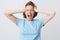 Portrait of crazy hysterical young woman in blue tshirt with closed eyes and hands on head looks stressed and screaming isolated