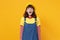 Portrait of crazy screaming girl teenager in french beret, denim sundress keeping eyes closed isolated on yellow