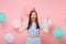 Portrait of crazy young woman in birthday hat and blue dress screming spreading hands on pastel pink background with