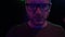 Portrait of creepy adult man in glasses looking in camera close up. Face of man standing with flashing colored lights on