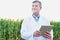 Portrait of Crop scientist wearing lab coat while using digital tablet against corn plant growing in field
