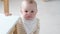 Portrait of curious child at home. Little baby peeks out from the table in kitchen and looks into camera. Happy