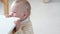 Portrait of curious child at home. Little baby peeks out from the table in kitchen and looks into camera. Happy