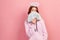 Portrait of curious curly haired teenage girl in hoodie with halo on head hiding face with bunch of dollar banknotes and looking