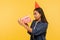 Portrait of curious happy brunette girl in denim shirt and funny cone hat opening birthday gift, looking inside