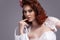 Portrait of Curious Redhaired Caucasian Female Posing in White Wedding Dress and Little Purse Against Gray Background