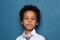 Portrait of curious smart black child boy student on blue background. African American kid pupil 6 years old