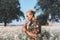 Portrait of curly blond guy is standing at the field and sniffs a flowers. Romantic, summer time. Flowers around and trees