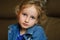 Portrait of a curly blue-eyed girl with a calm look. She is wearing a denim vest