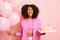 Portrait of curly haired woman with overjoyed expression celebrates birthday, holds tasty cake with burning candles