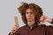 Portrait of a curly-haired young man with a wooden comb in magnificent hair dissatisfied with the result on a gray isolated