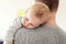 Portrait of cute adorable blond caucasian toddler boy sleeping on fathers shoulder indoors. Sweet little child feeling safety and