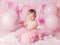 Portrait of cute adorable Caucasian baby girl with blue eyes in pink tutu skirt celebrating her first birthday with gourmet cake