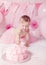 Portrait of cute adorable Caucasian baby girl with blue eyes in pink tutu skirt celebrating her first birthday with gourmet cake