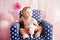 Portrait of cute adorable Caucasian baby girl with blue eyes sitting in blue children kids armchair with white stars celebrating